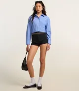 Camisa celeste con rayas verticales blancas, de corte alargado, cuello inglés y mangas largas.