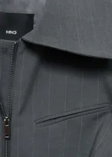 Chaqueta gris con finas rayas verticales, corte entallado, cuello camisero, cierre frontal con cremallera doble, bolsillo de ribete en el pecho y mangas largas.
