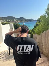 Remera color crema de corte recto y mangas cortas, con estampado en la espalda con el logo "ITTAI" en negro con líneas rojas, azules y blancas, y la leyenda "AN IBIZA PRODUCE. Ittai Stars Department Gallery - Ibiza Edition. If you're in Ibiza, 112 is not an option.".