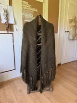 Ruana tejida a mano en lana merino 100%, color verde militar, con diseño de puntos calados y flecos largos en el ruedo.