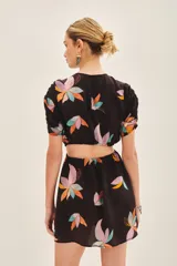 Vestido corto negro con estampado floral abstracto en tonos pastel (rosado, naranja, celeste, amarillo). Presenta cuello redondo, mangas cortas abullonadas y abertura horizontal en la cintura.