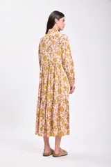 Vestido midi de corte holgado con estampado floral en tonos rosa y amarillo. Tiene cuello camisero, mangas largas con puños elásticos y falda escalonada.