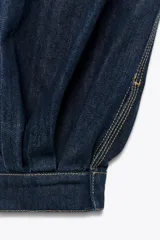 Pantalón bombacho de denim azul oscuro, tiro medio, con trabillas en la cintura, bolsillos delanteros y traseros, pespuntes marcados a contraste, bajo abullonado con puño y cierre frontal con cremallera, botón y ganchos metálicos.