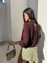 Camisa color borgoña con cuello clásico, cierre frontal con botones, bolsillo de parche con encaje en el pecho y mangas largas con lazo en los puños.