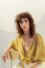 Blusa color mostaza de lino, con escote en V y mangas cortas abullonadas. Se ata en la parte delantera con dos cordones.