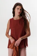 Top sin mangas color terracota con cuello redondo y bolsillo frontal. Presenta costuras a contratono en blanco que definen los bordes y el bolsillo.