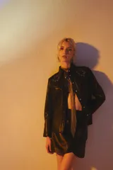 Minifalda negra de cuero ovino, corte al cuerpo, con cruce tipo pétalo en el frente y pinzas laterales que generan pliegues.