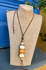 Colgante con cordón de cuero marrón y cuentas de cerámica color crema, naranja y marrón.
