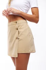 Falda short color beige con diseño cruzado y botones decorativos.
