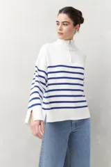 Polera blanca de punto con cuello alto y cierre metálico, de calce relajado y diseño a rayas horizontales azules.