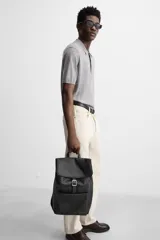 Mochila negra de cuero sintético, con solapa y cierre magnético. Tiene un compartimento principal con espacio para dispositivos electrónicos de hasta 13 pulgadas y un bolsillo con cierre. En la parte frontal cuenta con un bolsillo con cierre. Tiene asa de mano y dos asas de hombro ajustables y acolchadas.
