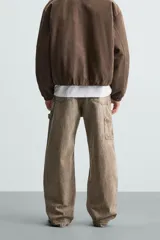 Pantalón gris de corte relaxed fit, con cinco bolsillos, efecto lavado, aplicación de tira y bolsillo multifunción en perneras. Cierre frontal con cremallera y botón.