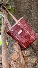 Bolso matero de cuero color marrón con textura símil cocodrilo, con costuras blancas y manijas de cuero color beige.