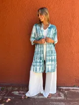 Camisa larga de manga tres cuartos, color verde azulado y blanco, con estampado tie-dye. Tiene cuello camisero, botones frontales y bolsillos en el pecho.