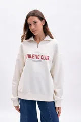Buzo de tejido de punto color blanco roto, con cuello polo y medio cierre frontal. Presenta una banda horizontal en el pecho con el texto "ATHLETIC CLUB" en color rojo.
