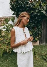 Conjunto de top y falda color crema, confeccionado en lino. El top es sin mangas, con detalle de lazos en el escote y volados en el ruedo. La falda es larga y de corte recto.