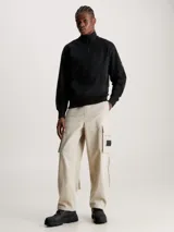 Buzo negro de felpa de algodón orgánico con cuello alto con cremallera, puños y bajo de canalé, bolsillo canguro y parche con logo en la manga.