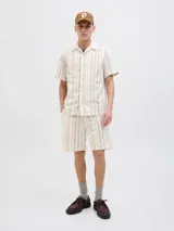 Camisa de manga corta con botones, cuello resort y corte relajado. Diseño a rayas verticales color beige y blanco.