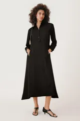 Vestido largo negro tipo camisero, confeccionado en viscosa. Tiene cuello solapa, manga larga con puños, bolsillos delanteros y cierre frontal con botones. Incluye cinturón ajustable con trabillas y botones.
