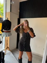 Vestido corto negro con estampado de pequeños lunares blancos. Presenta escote corazón con detalle de botones frontales y volados en las mangas cortas.