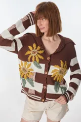 Cardigan tejido de punto color marrón con rayas horizontales blancas y bordado de flores amarillas. Tiene cuello marinero, cierre con botones de madera y corte holgado.
