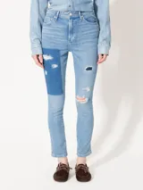 Jeans de tiro medio con calce slim y corte recto en el tobillo. Presenta roturas, lavados y parches de denim en diferentes tonos de azul.