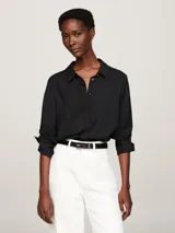 Camisa negra de viscosa con corte amplio, cuello inglés, tapeta de botones oculta, puños abotonados y logo metálico en la manga.