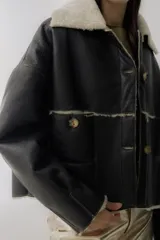 Campera corta de cuero color marrón oscuro con interior de piel sintética color crema. Tiene cuello con solapas, cierre frontal con botones a tono, dos bolsillos delanteros y puños con detalle de piel.