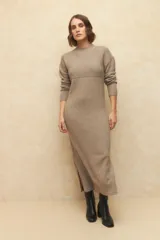Vestido de punto largo, color beige, elastizado y suave, con cuello alto y pequeñas aberturas laterales.