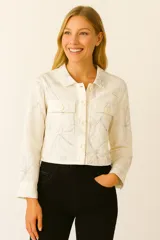 Chaqueta color crema con estampado de flores en color gris, de corte cropped, con cuello camisero, cierre frontal con botones a tono, mangas largas y bolsillos tipo parche en el pecho.