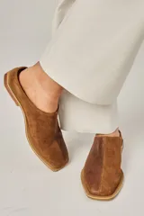 Zuecos color beige confeccionados en cuero vacuno, con punta cuadrada y suela plana color negro.
