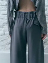 Pantalón sastrero gris con pinzas, tiro alto, corte palazzo y cierre frontal con doble botón.