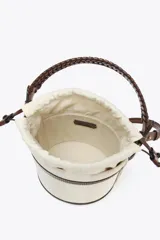 Bolso tipo bucket cilíndrico a rayas verticales en tonos beige y blanco, con asa de mano trenzada color marrón y asa de hombro extraíble. Incluye bolso de tela interior y pespuntes a contraste.