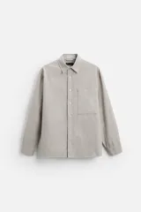 Camisa color crema de corte relaxed fit, confeccionada en tejido de mezcla de algodón suave al tacto. Tiene cuello solapa, manga larga con puños abotonados, un bolsillo de parche en el pecho y cierre frontal con botones.