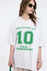 Remera blanca de algodón con cuello en V y estampado frontal con la frase 'Montevideo, UY', el número '10' y la leyenda '*Local* Championship' en color verde.