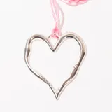 Collar con dije plateado en forma de corazón abierto, con detalle de pequeño corazón en una de las puntas. Cordón fino color rosa.