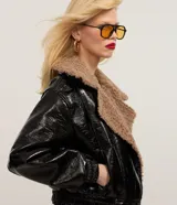 Campera biker negra de cuero sintético con efecto barnizado y cuello de peluche marrón. Tiene cierre delantero cruzado, mangas largas con puños ajustados y bolsillos laterales.