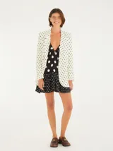 Vestido corto con estampado de lunares blancos sobre fondo negro, con escote profundo en V, mangas largas abullonadas y falda en capas con acabado en marias.