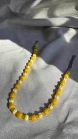 Collar corto de cuentas amarillas de diferentes formas y tamaños, con cierre de mosquetón y cadena de alargue plateada.