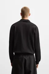 Polo de manga larga color negro, de punto tejido en hilatura de algodón, corte relaxed fit, con cuello solapa y cierre frontal de botonadura.