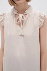 Blusa sin mangas color crudo con cuello con lazo y volados en los hombros.