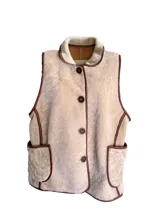 Chaleco color crema con cuello y borde de cuero marrón, con cierre de botones y bolsillos frontales.