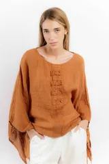 Blusa color ladrillo de lino con cuello redondo y mangas largas amplias. Presenta detalle de apliques rectangulares verticales en el frente.