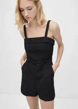 Mono corto negro de tejido mezcla de lana con tirantes anchos, cuello escotado, cinturón decorativo y cierre de cremallera invisible en la parte posterior.
