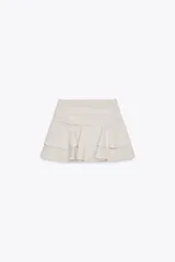 Falda pantalón color crema, de tiro medio, con volantes en capas y cierre lateral con cremallera.