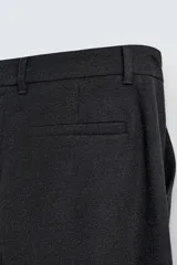 Pantalón de vestir negro, corte amplio, con pliegues en la cintura, bolsillos laterales y traseros de ojal.