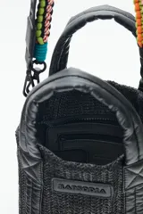 Cartera tote mini color negro, confeccionada en tejido tipo rafia. Cuenta con bolsillos internos, dos correas desmontables y abertura superior con cierre.