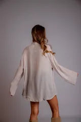 Camisa color beige claro, de corte holgado, con cuello clásico, cierre frontal con botones, mangas largas con puños abotonados y detalles de broderie en la parte delantera.