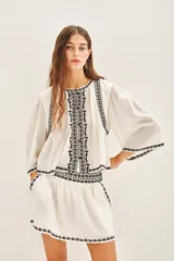 Camisa blanca de algodón con bordado negro en el ruedo, corte amplio y largo corto. Escote redondo y mangas largas abullonadas.