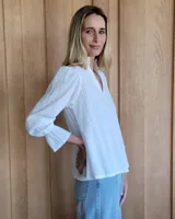 Blusa color beige con cuello con volados, mangas largas abullonadas con puños elásticos y cierre con botones en la parte delantera.